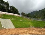 A grassy hill with a fence and a hill

Description automatically generated