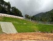 A grassy hill with a fence and a hill with trees in the background

Description automatically generated